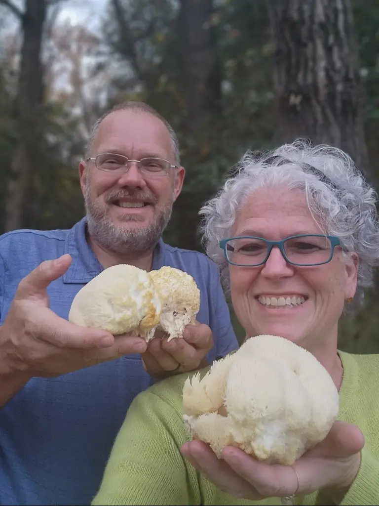 A man and woman stand together, each holding a lion's mane mushroom highlighting their successful mushroom foraging adventure.